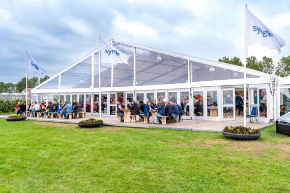 Large white event tent on a lawn with people seated at tables