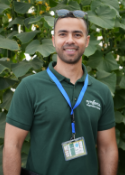 Smiling man in green polo with lanyard and ID badge, standing outdoors by leaves