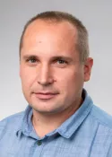 Studio headshot of a man in a light blue shirt against a gray background