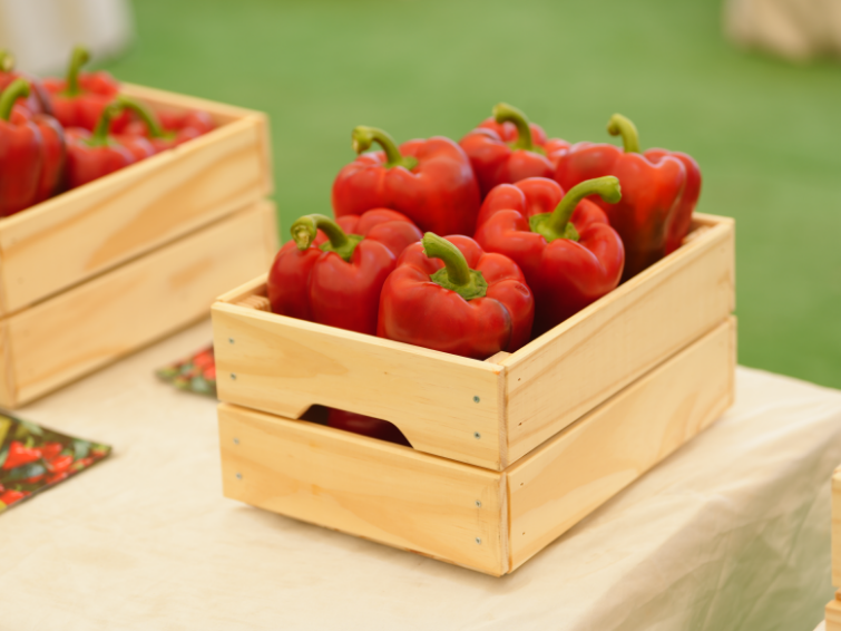 Wooden crate filled with red bell peppers on a table outdoors