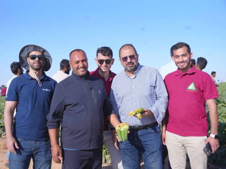Five men posing outdoors on a sunny day, one holding a yellow item