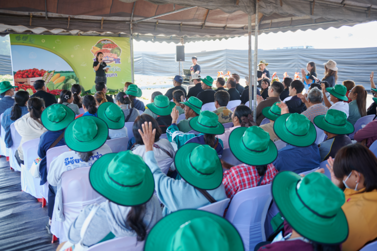 Crowd in green hats raising hands at an outdoor event under a canopy