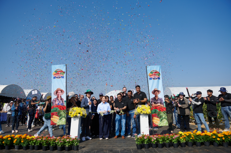 Group of people at a memorial ceremony with wreaths and balloons under a blue sky