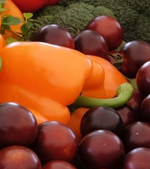 Assorted fresh produce: bell peppers, broccoli, cherry tomatoes, and grapes on a table