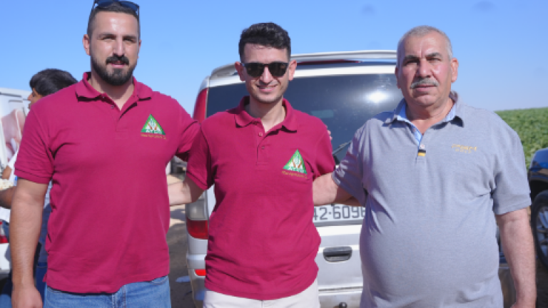 Three men in matching pink polos and gray shirt standing in front of a van outdoors