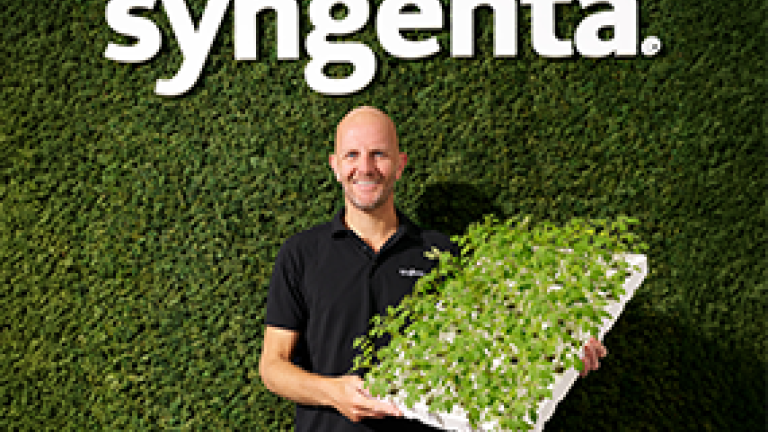 Syngenta logo above a man holding a tray of green seedlings against a leafy wall