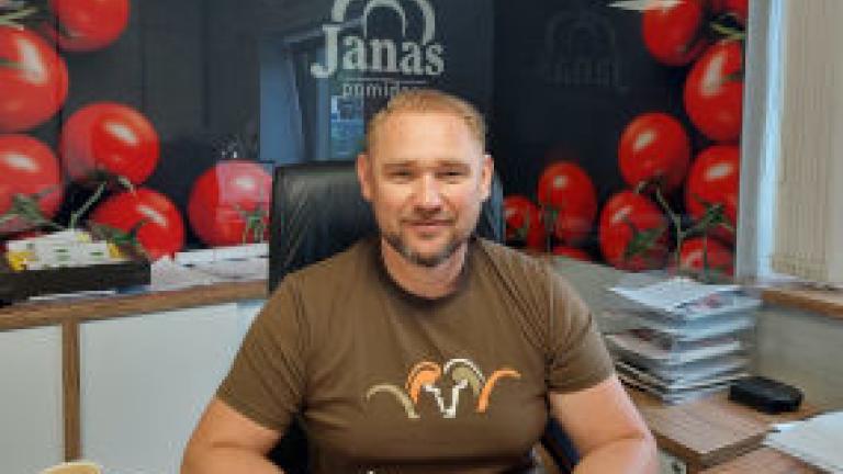 Man smiling at desk in office, with red balloons and “Janas” sign behind him