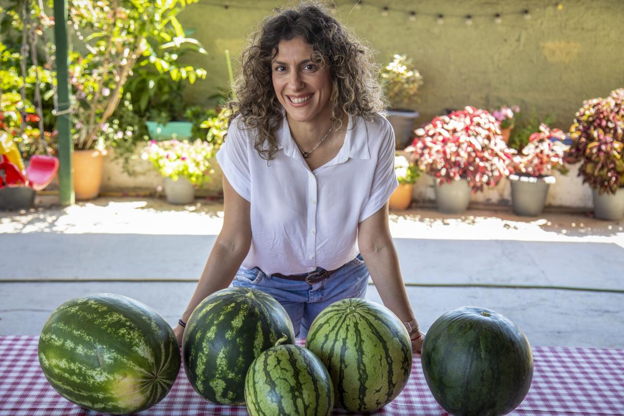 Smiling woman behind table with several watermelons outdoors